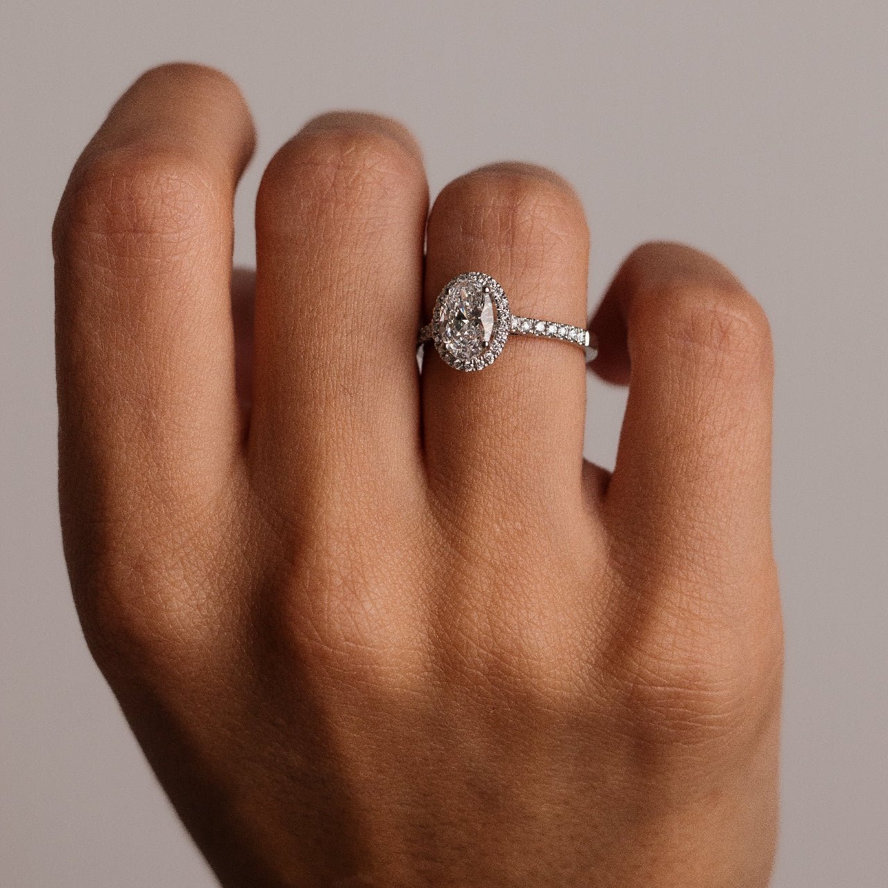 Diamond ring on a person's finger against a neutral background