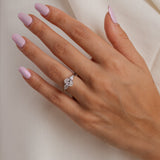 Hand with pink nail polish wearing a diamond ring on a neutral background