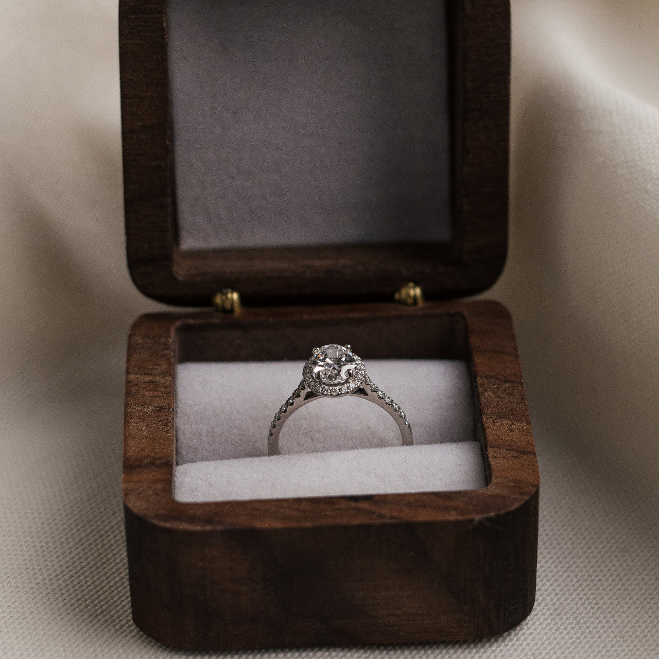Wooden ring box with a diamond ring inside on a neutral background