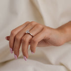 Hand wearing a diamond ring on a neutral background