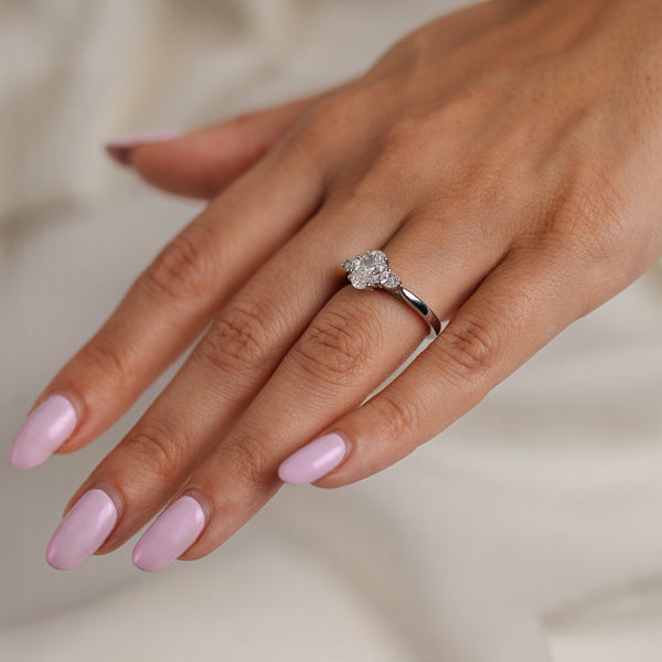 Hand wearing a diamond ring with pink nail polish on a neutral background