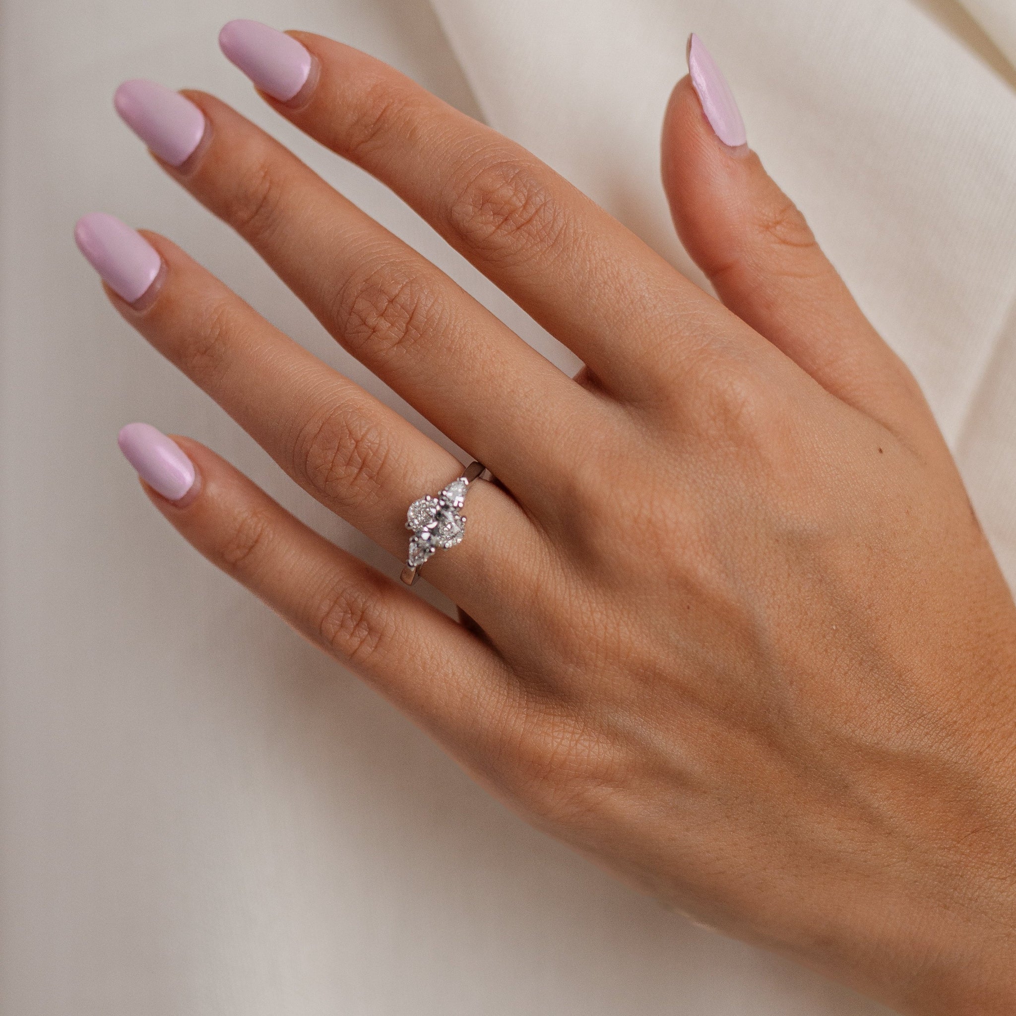Hand with pink nail polish wearing a diamond ring on a neutral background