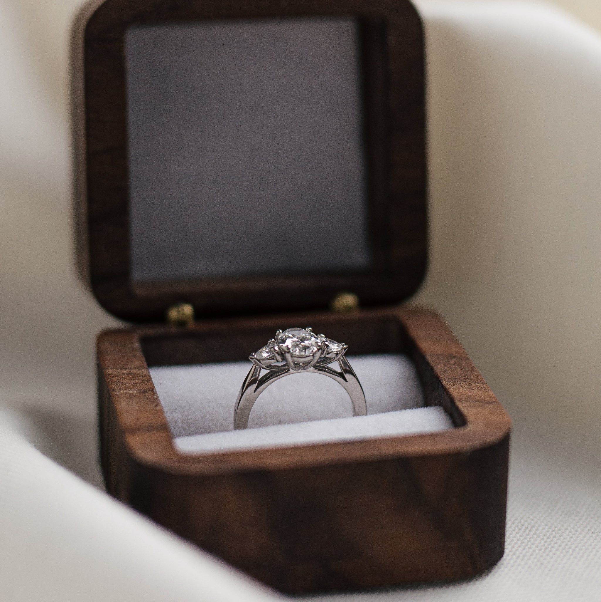 Trilogy diamond ring in a wooden box on a light background