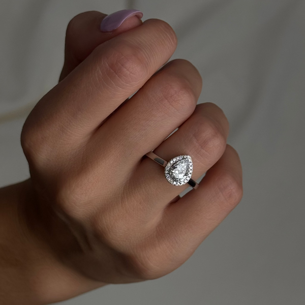 Hand wearing a halo diamond ring with a blurred background