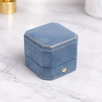 AtelierRings blue velvet octagonal ring box with gold trim detail on a marble surface for proposal presentation