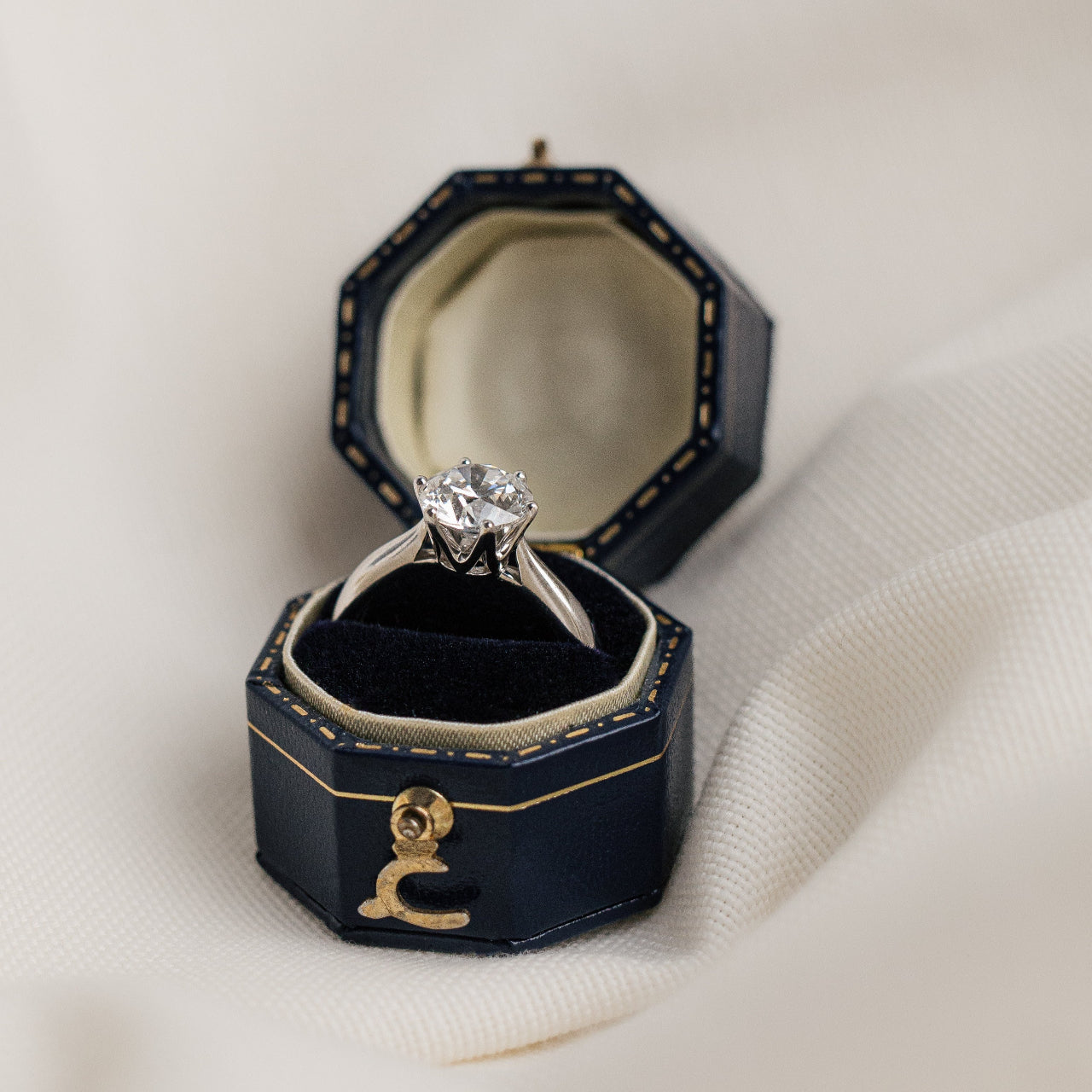 Diamond ring in a black hexagonal jewelry box on a white fabric background