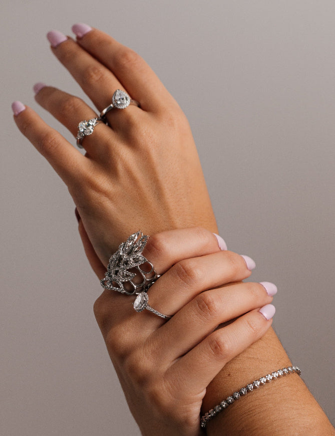 Hand wearing multiple silver rings on a neutral background