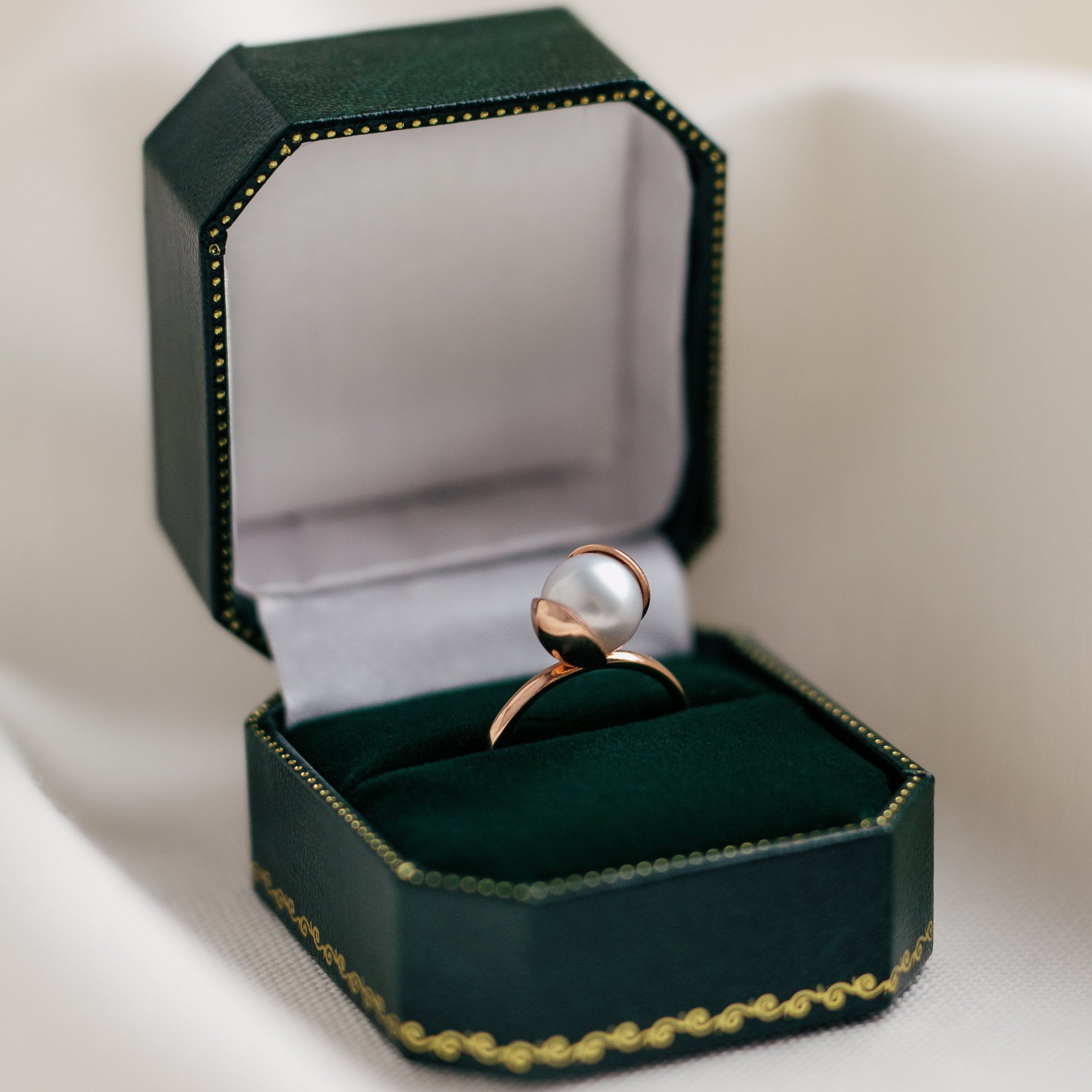 Rose gold ring with a pearl in a green jewelry box on a white background