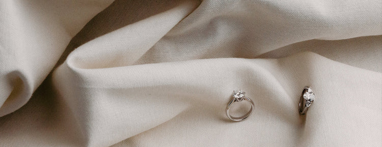 Two diamond rings on a textured beige fabric surface