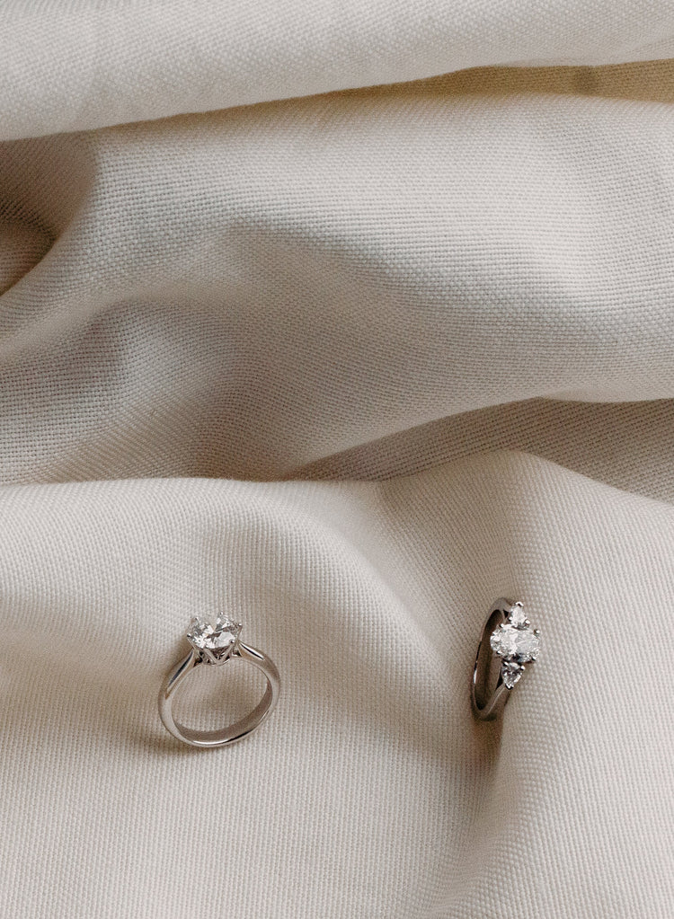 Two diamond rings with gemstones on a beige fabric background