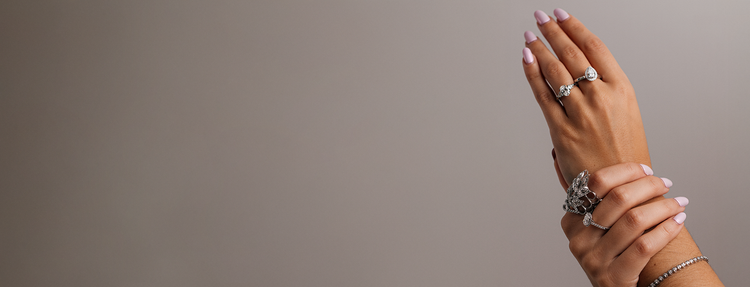 Hand model wearing multiple diamond rings on a plain background