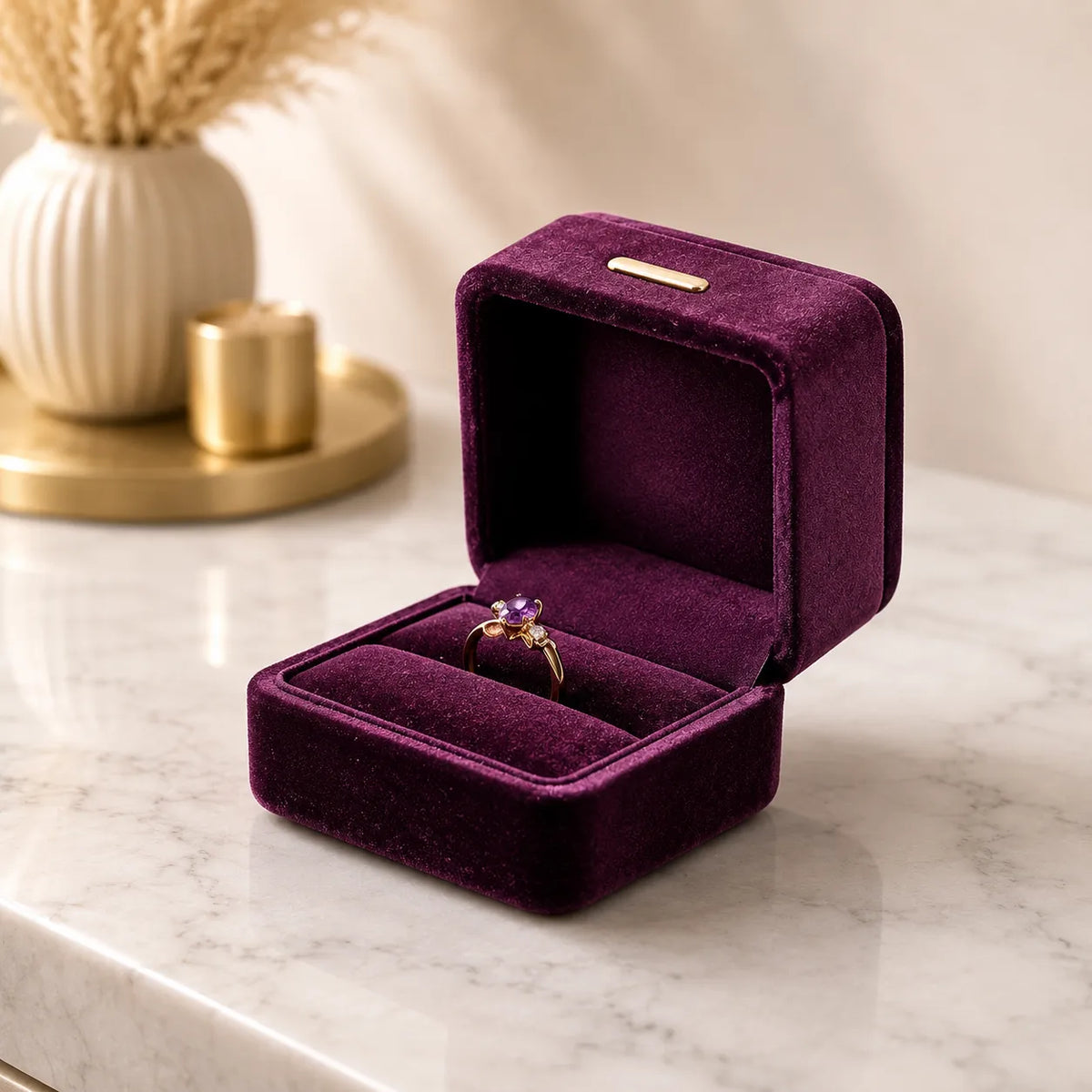 A purple velvet ring box with a gold clasp, shown open on a light marble surface. A gold ring with a purple gemstone is displayed inside the box.